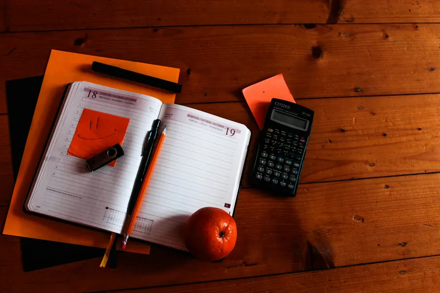 An open notebook, a pen and a scientific calculator on a wooden desk
