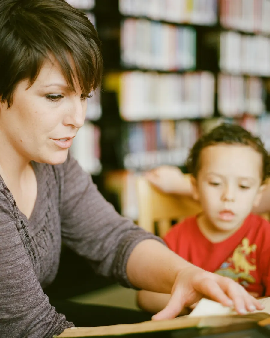 A woman reading with a young boy at a library table